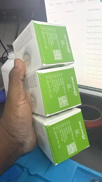 Sealed CGM sensor boxes held in one hand by the person who answers the phone here